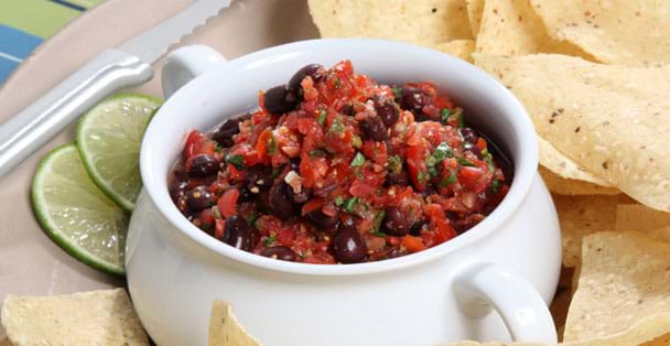 A bowl of black bean salsa with a tomato slicer on