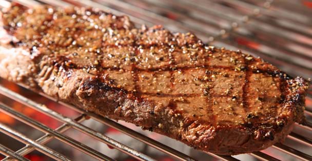 Close up of peppered strip steak on a grill.